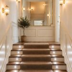 An enclosed stairway with layered lighting, light walls and a stair runner