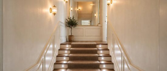 An enclosed stairway with layered lighting, light walls and a stair runner